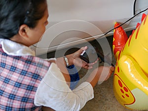 Woman`s hands holding and using mini air pump, connected to the car plug, to inflate a rocking doll