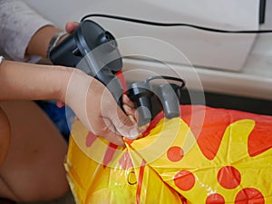 Woman`s hands holding and using mini air pump, connected to the car plug, to inflate a rocking doll