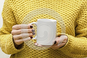 Woman's hands holding white blank cup mug of coffee,tea,hot beverage.female in yellow warm sweater