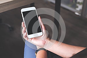 Woman`s hands holding white mobile phone with blank black desktop screen