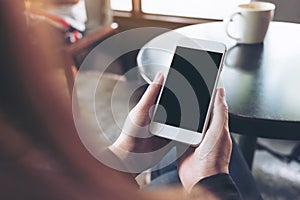 Woman`s hands holding white mobile phone with blank black desktop screen in cafe