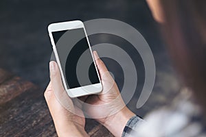 Woman`s hands holding white mobile phone with blank black desktop screen in cafe