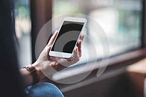 Woman`s hands holding white mobile phone with blank black desktop screen in cafe