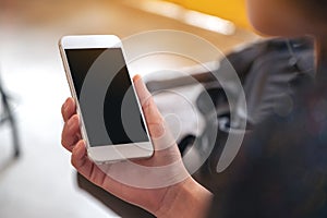 Woman`s hands holding white mobile phone with blank black desktop screen while drinking coffee in cafe