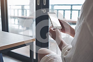 A woman`s hands holding white mobile phone with blank black desktop screen in loft cafe