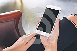 Woman`s hands holding white mobile phone with blank black desktop screen while sitting in cafe