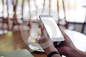 A woman`s hands holding white mobile phone with blank desktop screen in cafe