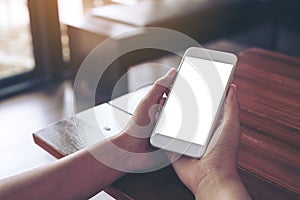 Woman`s hands holding white mobile phone with blank desktop screen on wooden table