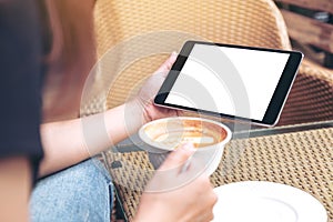 Mockup image of woman's hands holding tablet with blank screen while drinking coffee in modern cafe