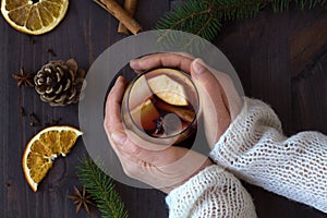 Woman`s hands holds hot mulled wine in a glass with orange and spices on wooden background. winter collection. top view