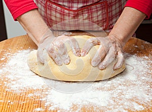 Woman's hands knead dough on wooden table