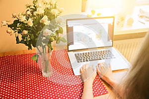 Woman`s hands on the laptop. Beautiful flowers and linen tablecloth. Perfect working place at home. Freelance concept. Searching