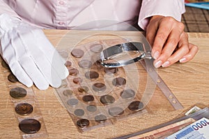 Woman`s hands with magnifying glass and a collection of coins