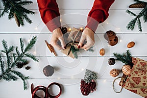 Woman`s hands making a Christmas present on white wooden table.