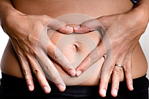 Woman& x27;s hands making a heart shaped symbol over the belly button symbolizing pregnanc