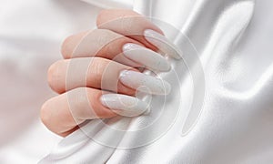 A woman\'s hands with a manicure on them, the nails are painted in a white color