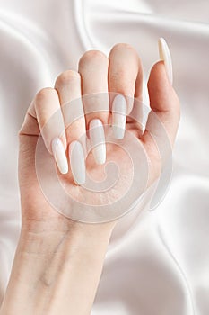 A woman\'s hands with a manicure on them, the nails are painted in a white color