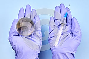 Woman`s hands in medical gloves is holding a planet earth globe and a syringe