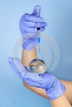 Woman's hands in medical gloves is holding a planet earth globe and a syringe
