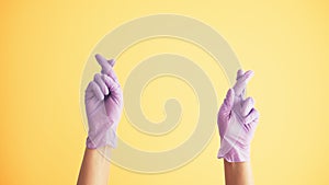 Woman`s hands in medical protective latex gloves praying with crossed fingers