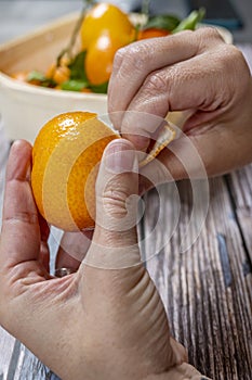 woman's hands peeling tangerines on unvarnished wooden table