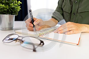 Woman`s hands with pen writing on notebook. Modern office desk.