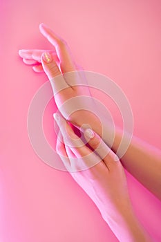 Woman`s hands with perfect manicure in trendy neon light on pink background.