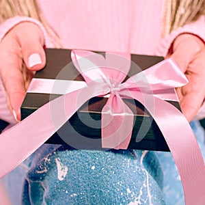 Woman`s hands with pink manicure holding black present box