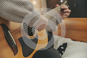 A woman`s hands playing guitar in a cozy bedroom.