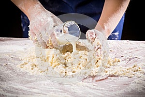 Woman`s hands pour the milk to dough for kneading