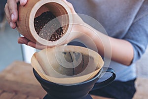 Woman`s hands pouring coffee grounds from wooden grinder into a drip coffee filter