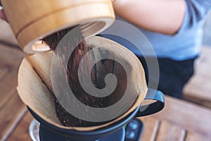 Woman`s hands pouring coffee grounds from wooden grinder into a drip coffee filter