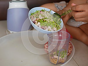A woman`s hands preparing / putting food ingredients in a small blender cup for blending for cooking food at home