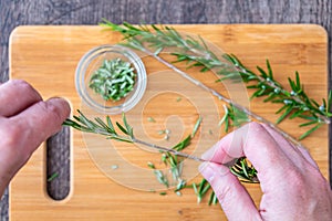 WomanÃ¢â¬â¢s hands pulling fresh rosemary leaves off a sprig, sprigs of rosemary with on a bamboo cutting board, chopped rosemary, pa