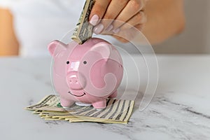 a woman\'s hands put dollar paper money in a piggy bank, next to a calculator on the table. economy, crisis and