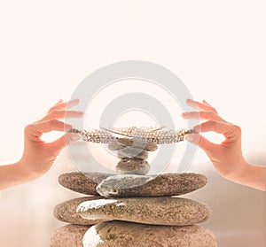 Woman`s hands put a feather on a pyramid of stones. Equilibrium, Balance concept. Zen stones on white