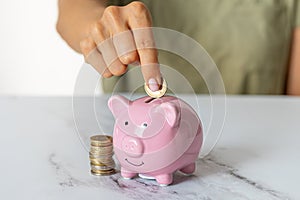 a woman's hands putting a euro coin in a piggy bank, saving money in a crisis and inflation
