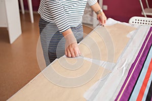 Woman`s hands with red nail polish palming a piece of tissue with a pattern. Concept of sewing