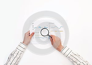 Woman`s hands are reviewing a report with graphs on a white table