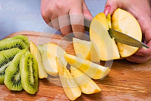 Woman`s hands slicing apple and kiwi