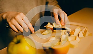 A woman's hands slicing an apple with a knife to prepare a dinner dessert - charlotte. The home cooking