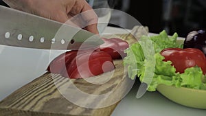 Woman`s hands slicing sweet Red Bell Pepper on a wooden cutting board. Cutting vegetables on a kitchen table