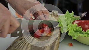 Woman`s hands slicing sweet Red Bell Pepper on a wooden cutting board. Cutting vegetables on a kitchen table