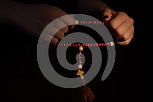 Woman`s hands stretching rosary with red beads.