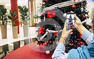 Woman`s hands take picture of the beautiful christmas tree in the shopping mall - concept of holidays and consumerism