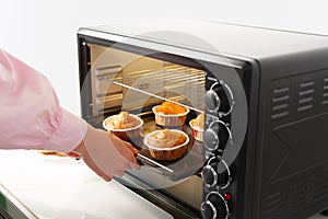 Woman& x27;s hands taking buscuit cupcakes out of mini oven