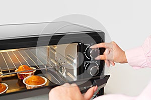 Woman's hands taking buscuit cupcakes out of mini oven photo