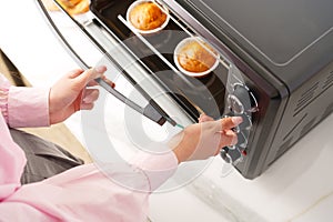 Woman& x27;s hands taking buscuit cupcakes out of mini oven photo