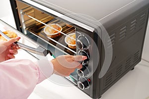Womans hands taking buscuit cupcakes out of mini oven photo