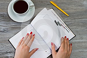 Woman`s hands turning a page in a notebook. Cup of tea and a pen